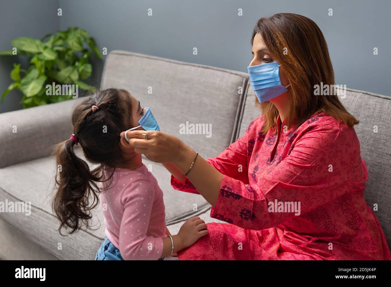 UNE MÈRE PORTANT UN MASQUE AIDANT LA FILLE À PORTER UN MASQUE POUR SÉCURITÉ Banque D'Images