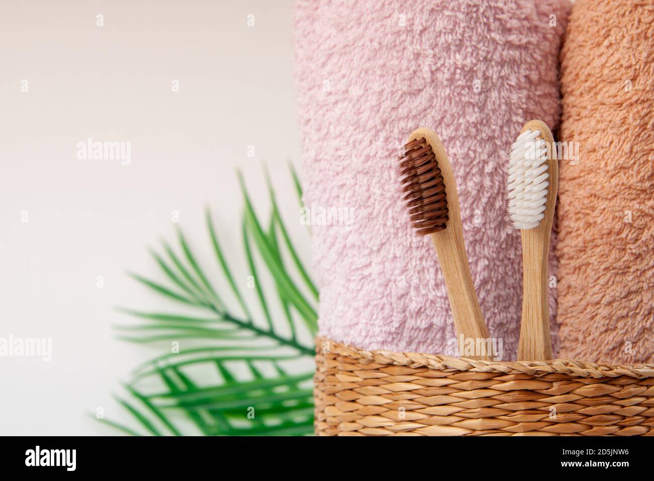 Brosses à dents en bambou avec serviettes dans un panier en bois d'osier et feuilles de palmier avec espace de copie sur fond blanc. Spa, mode de vie sain et écologie conc Banque D'Images