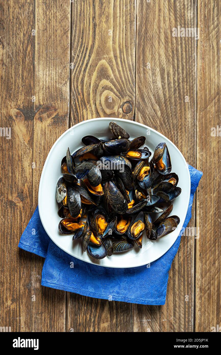 Délicieuses moules fraîches cuites à la vapeur dans une sauce au vin blanc avec persil dans une plaque blanche sur une table en bois Banque D'Images