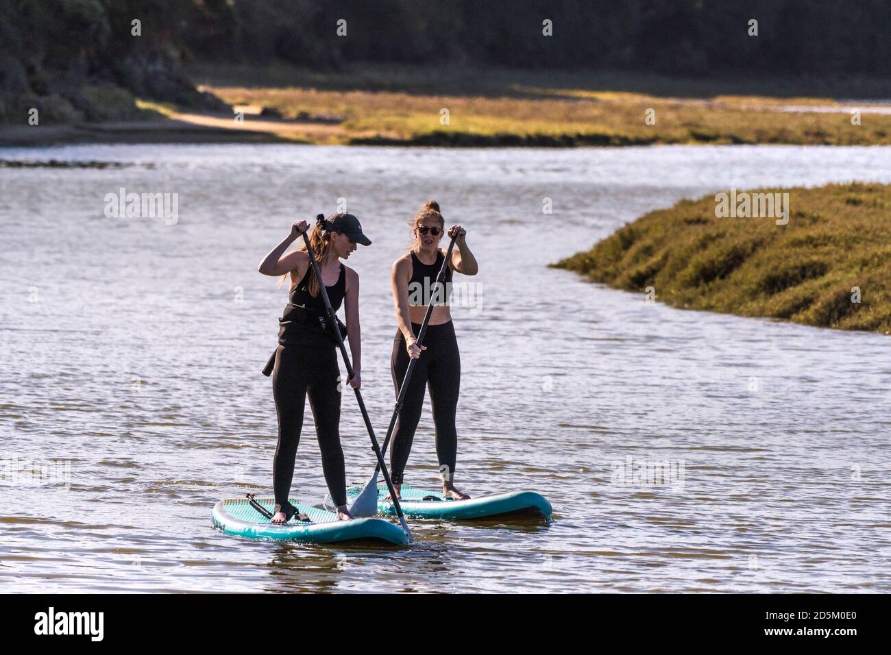 Deux femmes en vacances debout sur des planches à pédales Stand Up et pagayant sur la rivière Gannel à Newquay, en Cornouailles. Banque D'Images