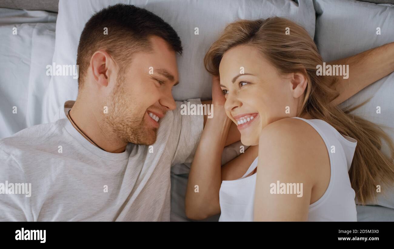 Joyeux jeune couple se câliner ensemble dans le lit, la jeune femme est enceinte et affectueuse des touches de partenaire et caresse sa tendresse. Vue de dessus. Banque D'Images