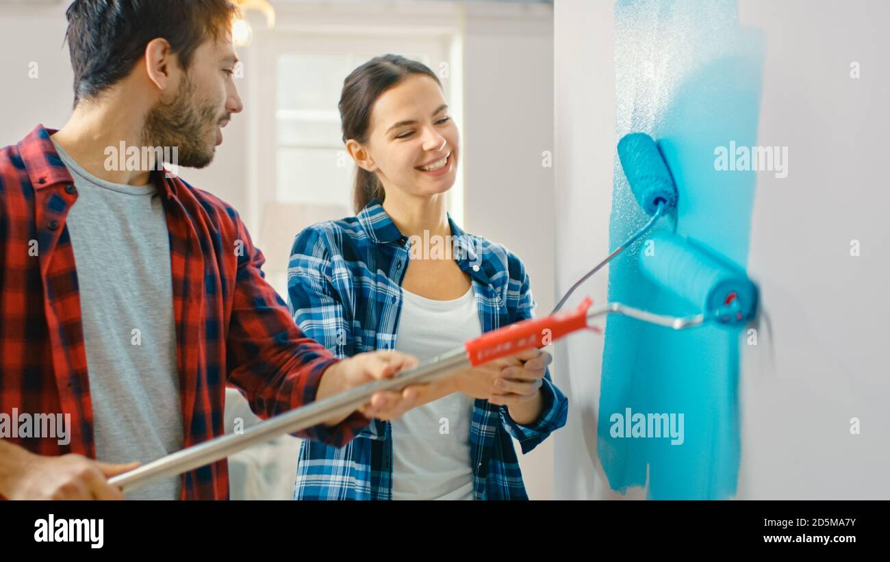 Jeune beau couple décorent leur nouvel appartement. Mari et femme peint le mur avec des rouleaux qui sont trempés dans la peinture bleu clair Banque D'Images