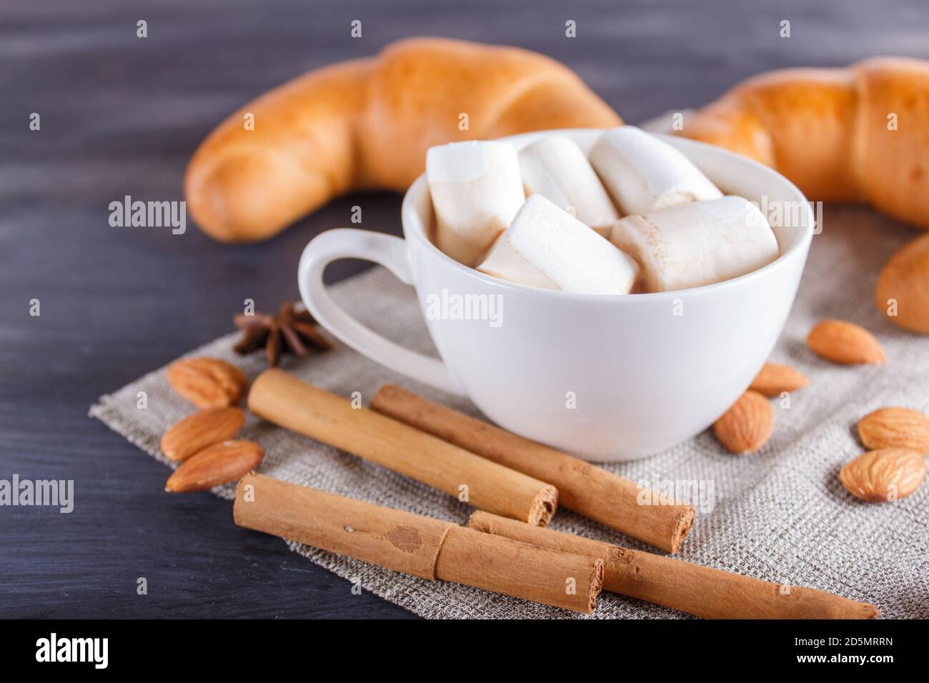 une tasse de chocolat chaud avec guimauve, croissants et épices sur serviette en lin et fond en bois noir. gros plan, espace copie. Banque D'Images