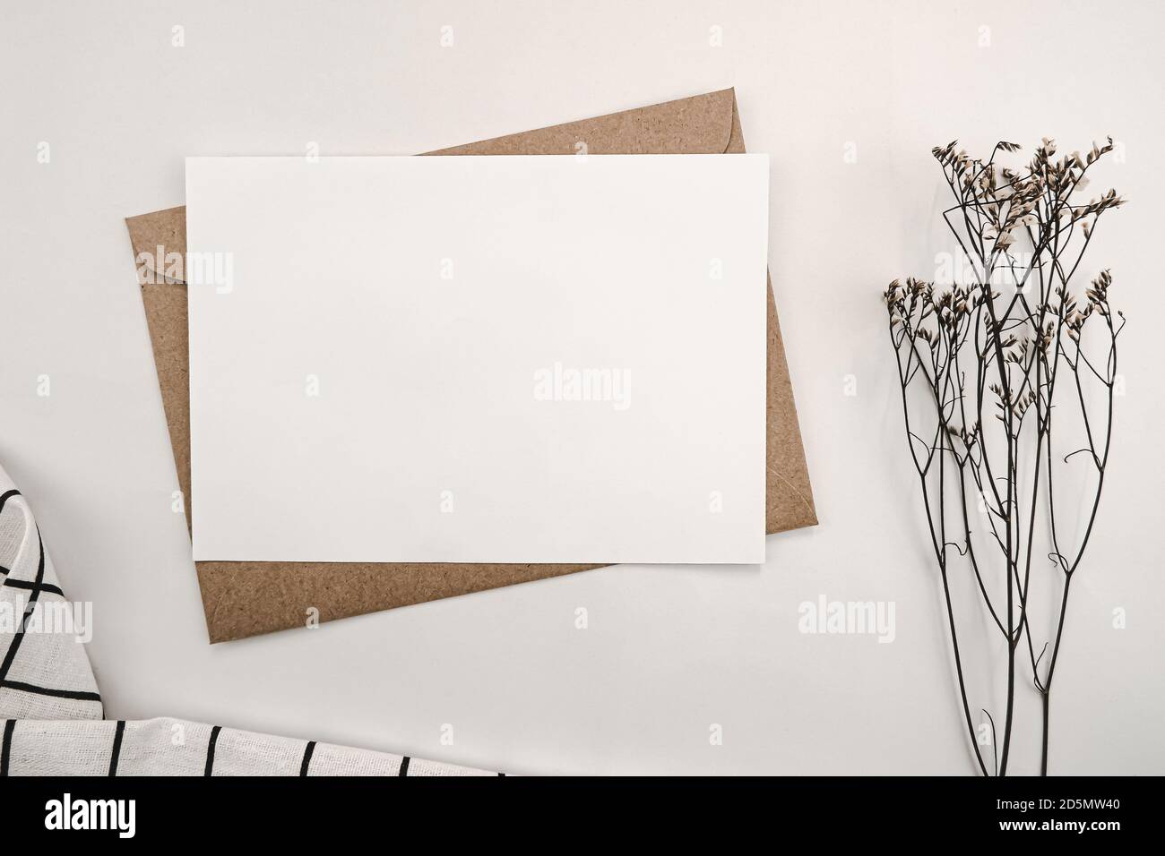 Papier blanc vierge sur enveloppe en papier marron avec fleur sèche de Limonium et tissu blanc avec motif de grille noir. Maquette de carte de vœux vierge horizontale. Banque D'Images