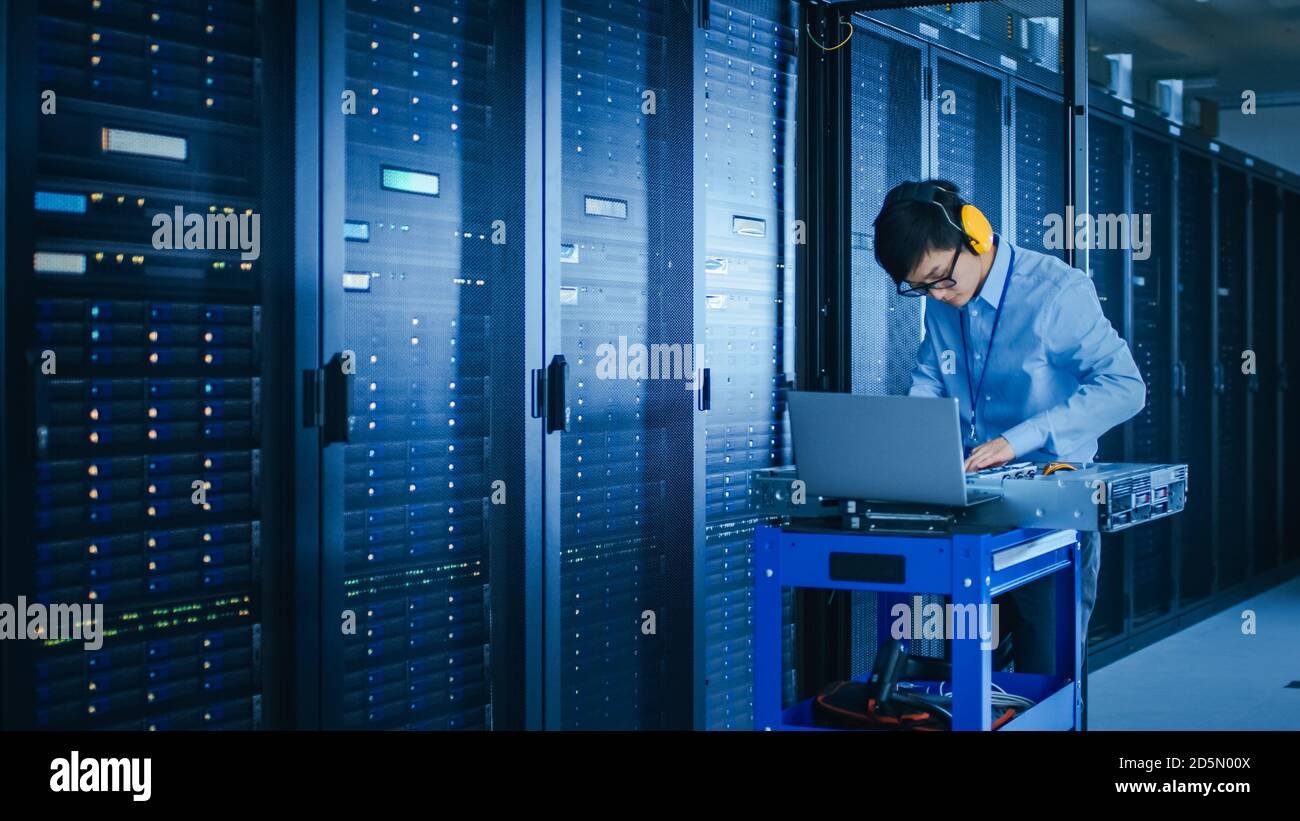 Dans le centre de données moderne : technicien INFORMATIQUE portant un casque de protection travaillant avec des racks de serveurs, sur un chariot-poussoir installant un nouveau matériel. Ingénieur Banque D'Images