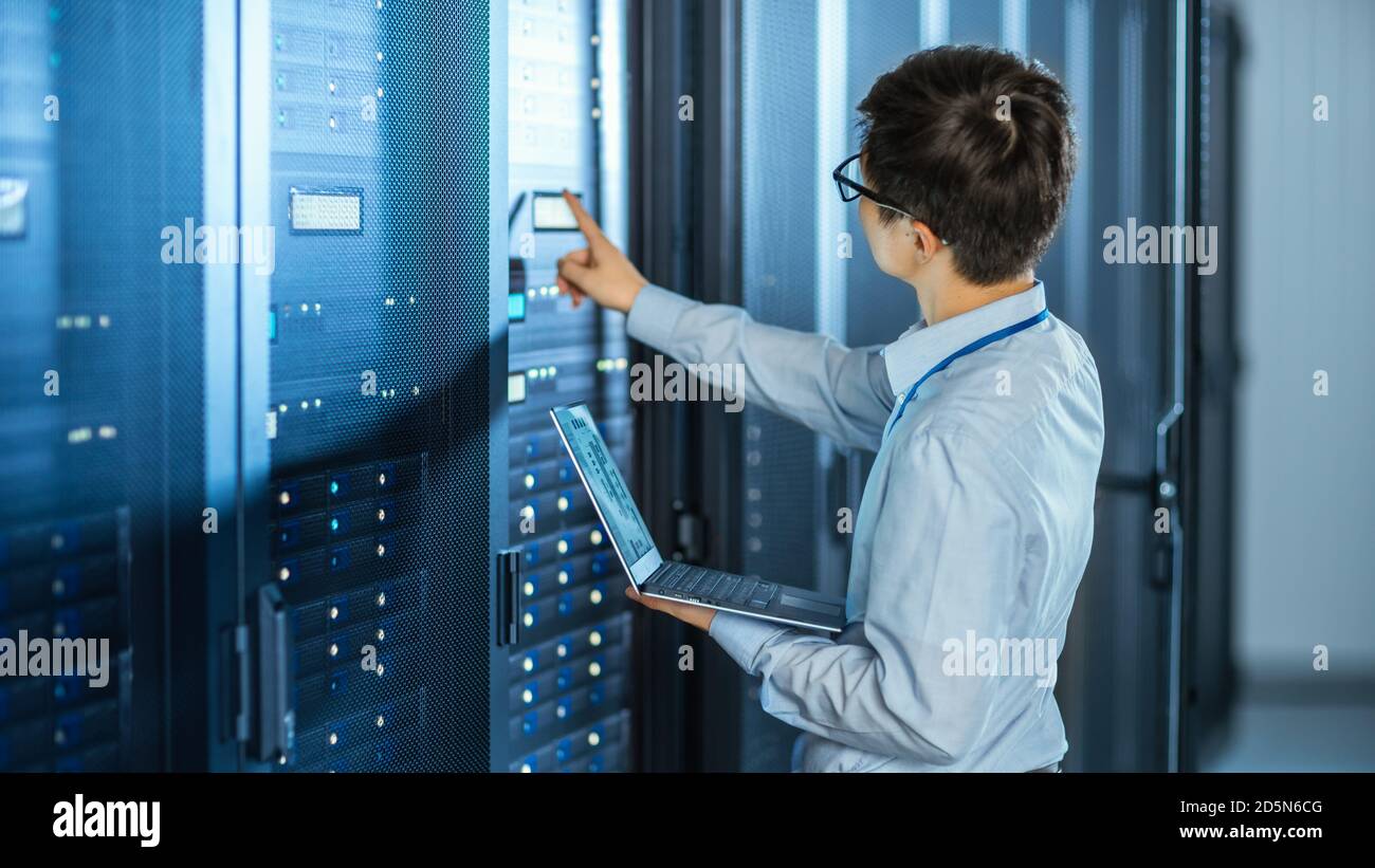 Dans le centre de données moderne : l'ingénieur INFORMATIQUE se trouve à  côté des armoires rack de serveur ouvertes, effectue la procédure de  maintenance et de diagnostic sans fil avec un ordinateur