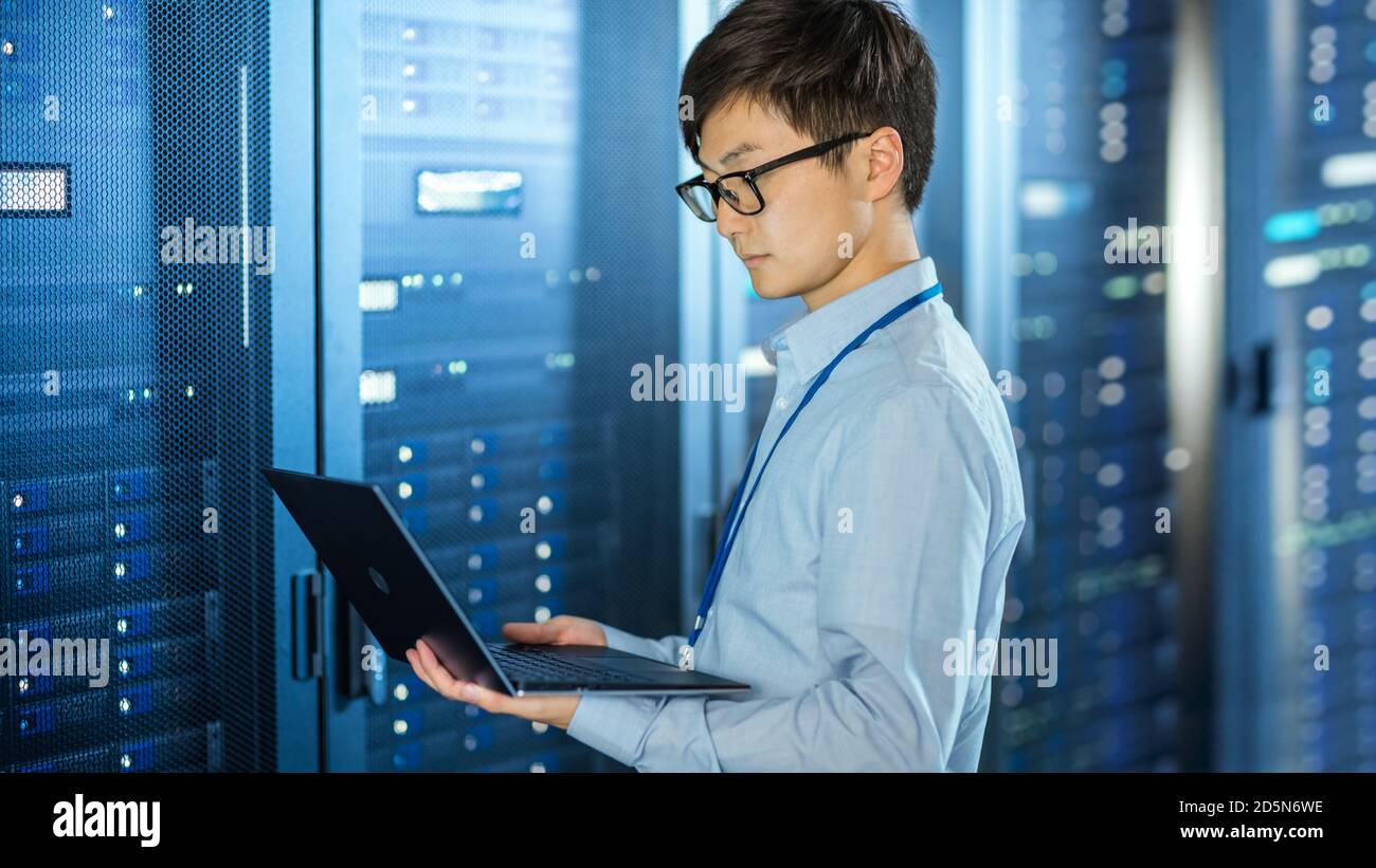 Dans le centre de données moderne : l'ingénieur INFORMATIQUE se trouve à côté des armoires rack de serveur, effectue la procédure de maintenance et de diagnostic sans fil avec un ordinateur portable. Banque D'Images
