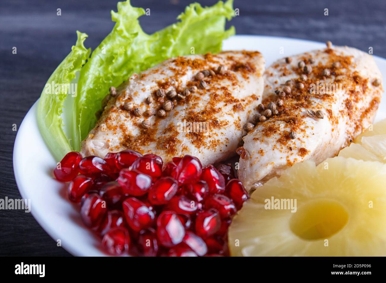 Filets de poulet frits avec laitue, ananas et graines de grenade sur fond de bois noir, espace de copie, gros plan. Banque D'Images