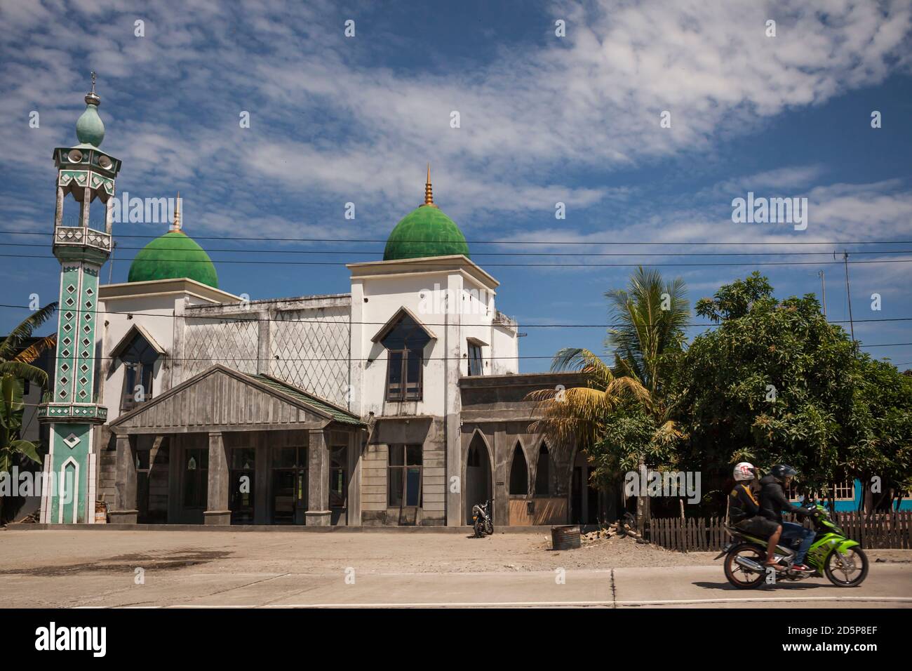 Plan horizontal de deux personnes sur une moto passant devant une mosquée, Sulawesi Sud, Indonésie Banque D'Images