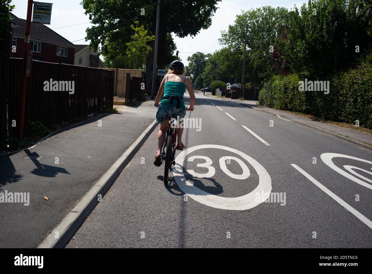 Une femme d'âge moyen en bonne santé fait du vélo sur une route peinte à 30 km/h habillée de vêtements d'été lors d'une balade à vélo. Banque D'Images
