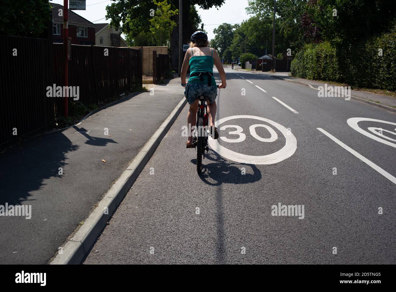 Une femme d'âge moyen en bonne santé fait du vélo sur une route peinte à 30 km/h habillée de vêtements d'été lors d'une balade à vélo. Banque D'Images
