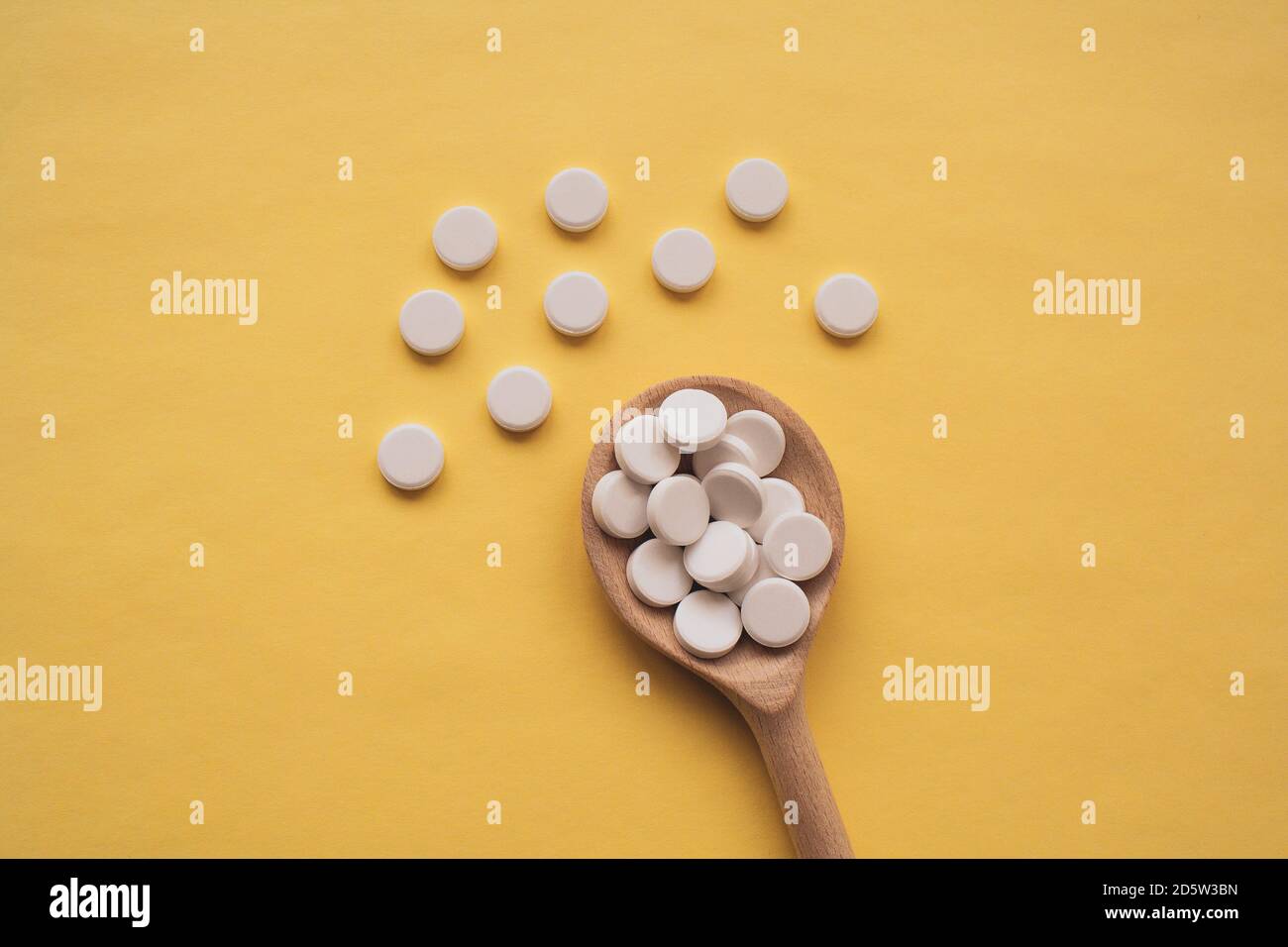 Comprimés blancs ronds sur une cuillère en bois sur fond jaune, les comprimés sont dispersés au centre de bas en haut Banque D'Images