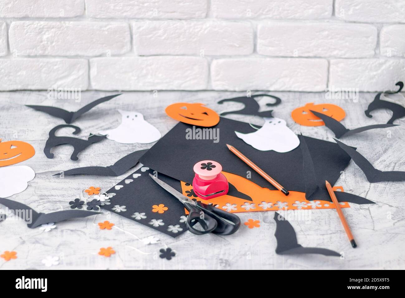 Préparation pour Halloween Décoration pour les fêtes, découpe de papier de couleur sur un mur de briques blanches. Papier de couleur orange et noir, ciseaux, crayons, perforatrice figurée mise au point douce. Banque D'Images