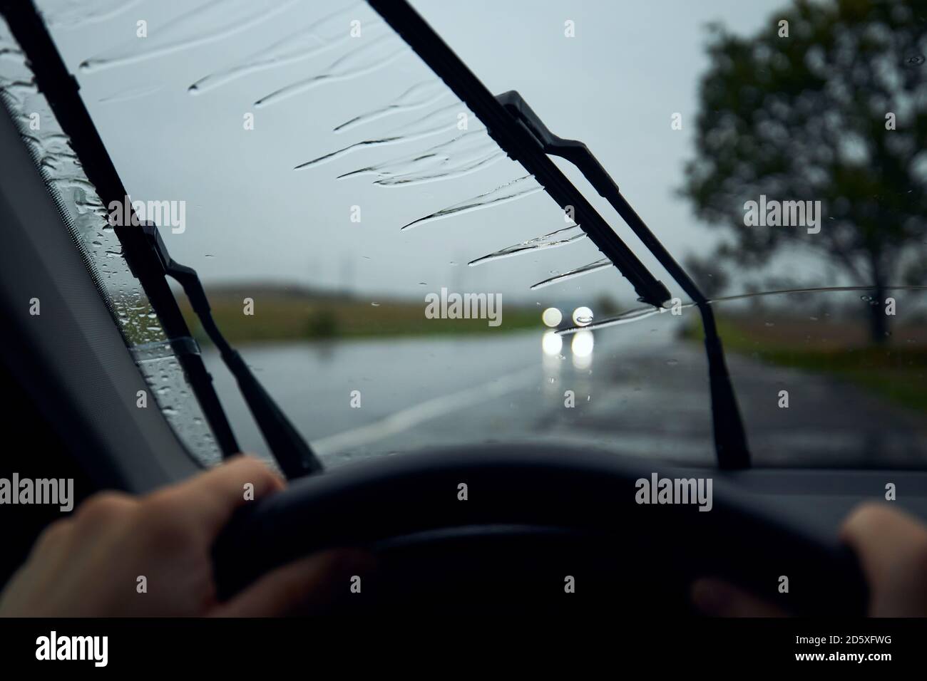 Conduite par forte pluie. Gouttes de pluie sur le pare-brise de la voiture contre la circulation au carrefour. Banque D'Images