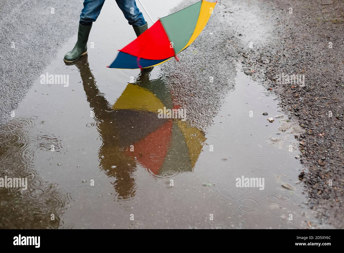 Petit garçon avec parapluie et bottes en caoutchouc debout dans une flaque, vue partielle Banque D'Images