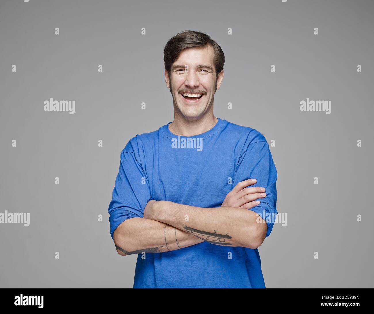 Portrait de l'homme en train de rire avec les bras croisés devant arrière-plan gris Banque D'Images