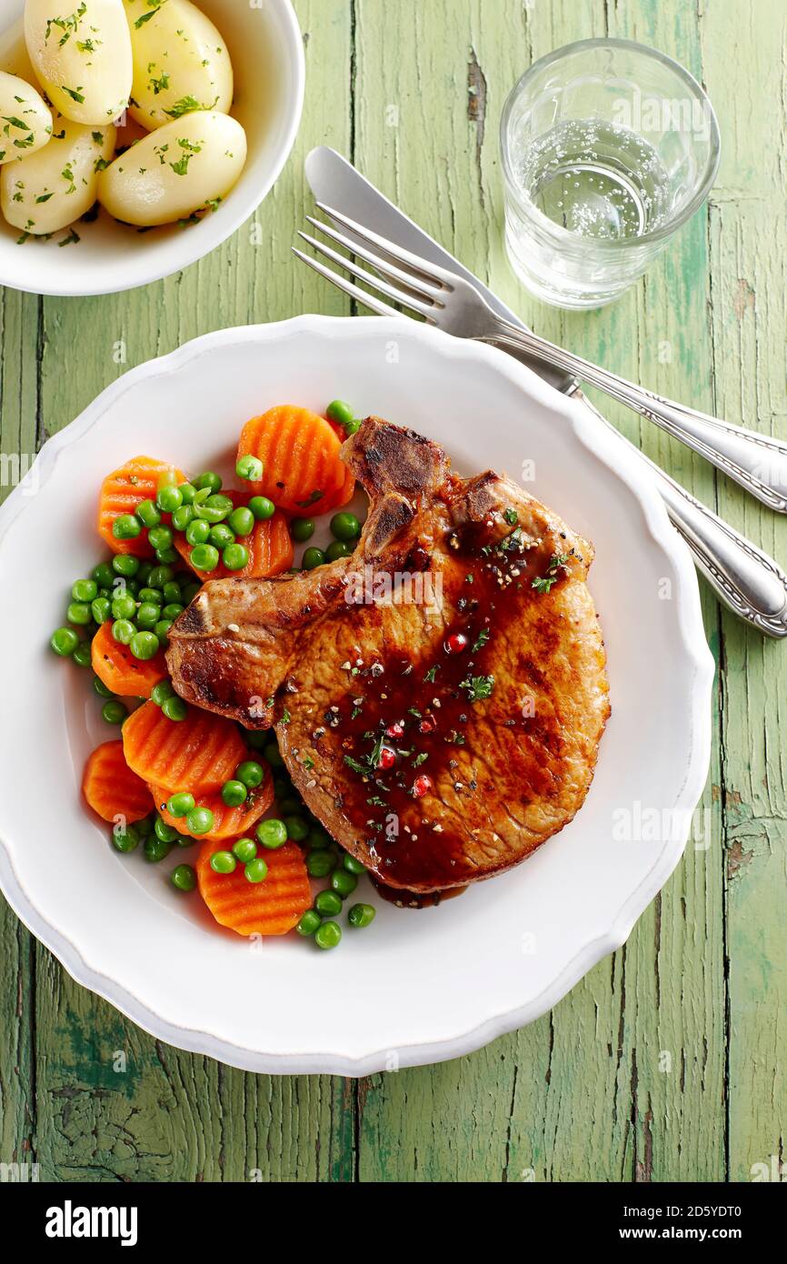 Côte de porc avec des carottes, des petits pois et des pommes de terre sur la plaque Banque D'Images