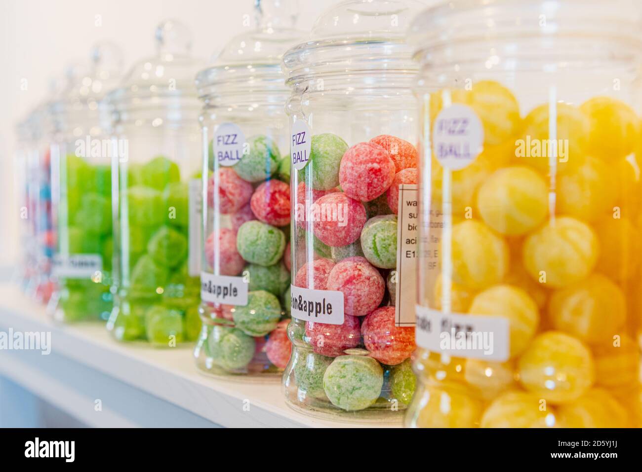 Bocaux en verre étiquetés de sucreries vertes, jaunes, rouges et bleues sur une étagère blanche dans un magasin de sucreries. Banque D'Images