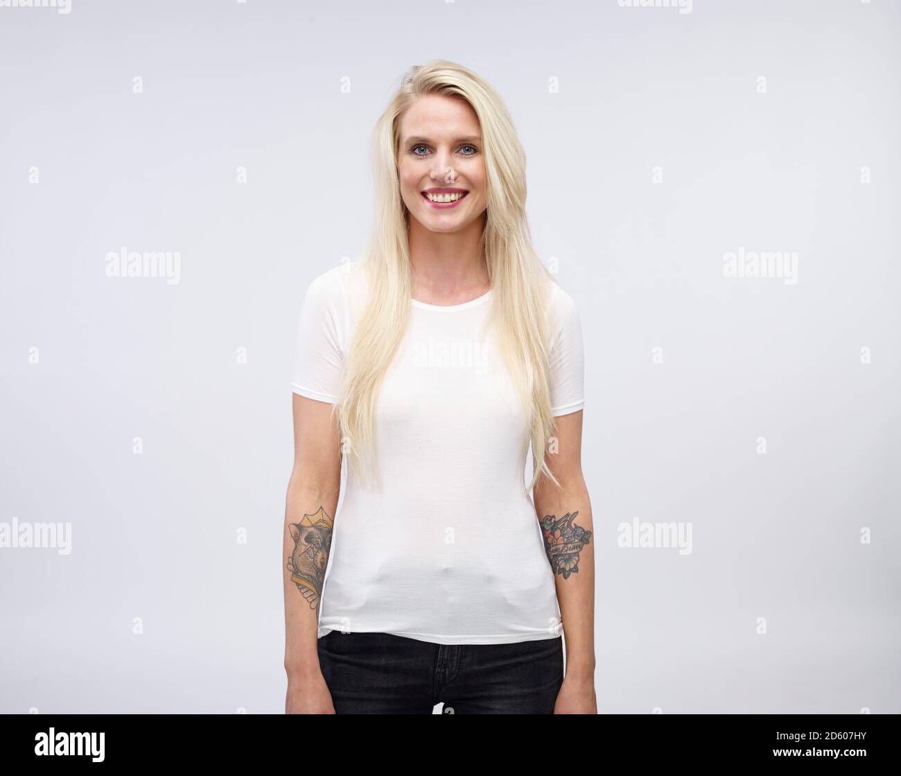 Portrait of smiling blonde jeune femme avec tatoo à ses avant-bras en face de fond clair Banque D'Images
