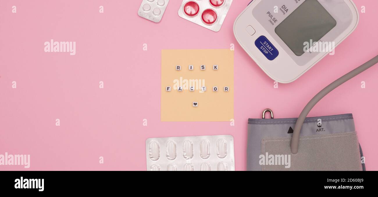 Concept de santé, cardiologie, maladie cardiaque. Les mots « FACTEUR DE RISQUE » sur les blocs. Moniteur de tension artérielle, comprimés sur fond rose. Vue de dessus, f Banque D'Images
