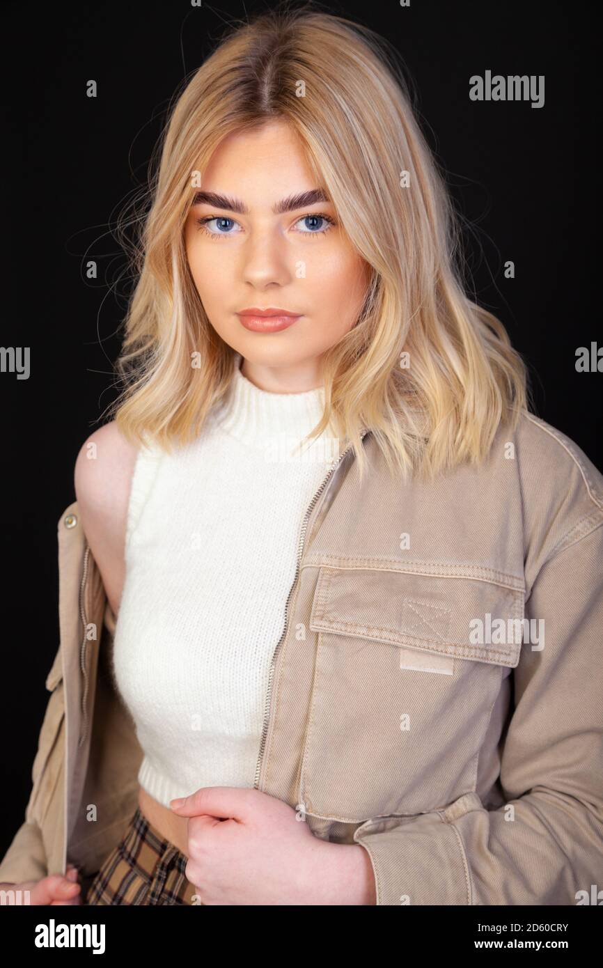 Une belle jeune femme blonde dans ses premières années de la vingtaine portant une veste brune et regardant directement l'appareil photo. Banque D'Images