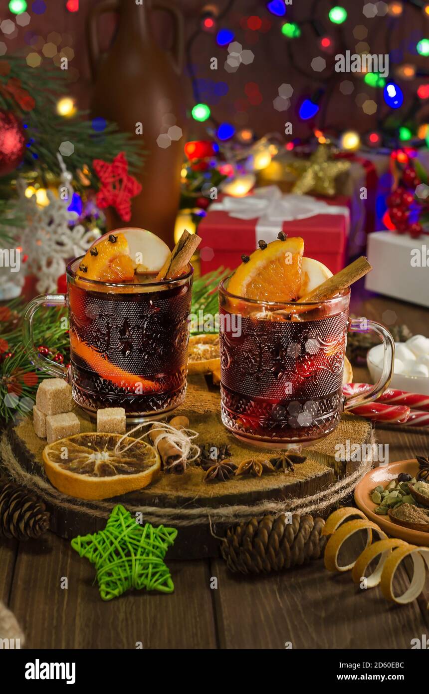 Vin chaud avec tranche d'orange, bâton de cannelle sur fond de guirlande lumineuse festive. Style sombre Banque D'Images