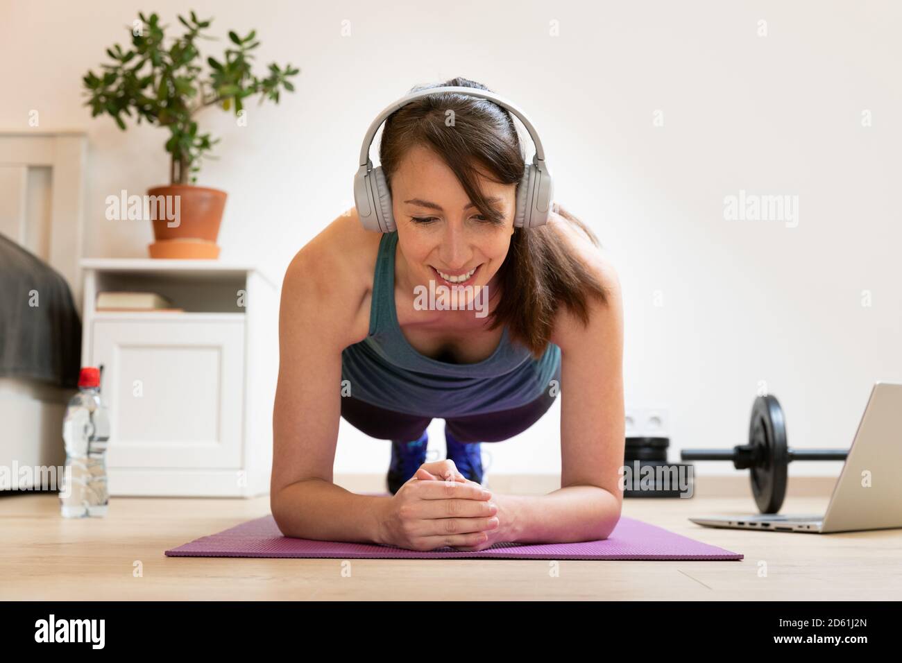 De belles femmes qui font de la remise en forme à la maison près du lit et regarder des tutoriels en ligne sur ordinateur portable dans la lumière naturelle. Concept de sport et de loisirs. Banque D'Images