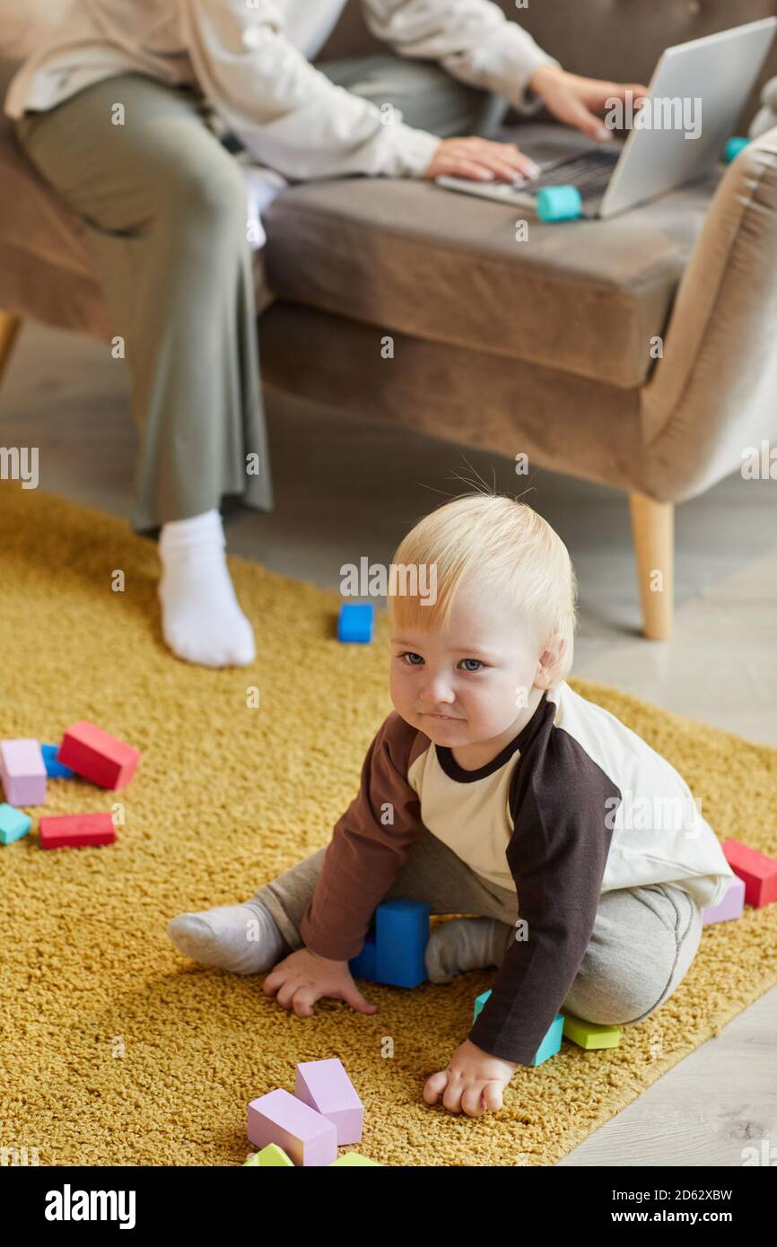 Bébé garçon mignon assis sur le sol et jouant avec blocs colorés dans la chambre Banque D'Images