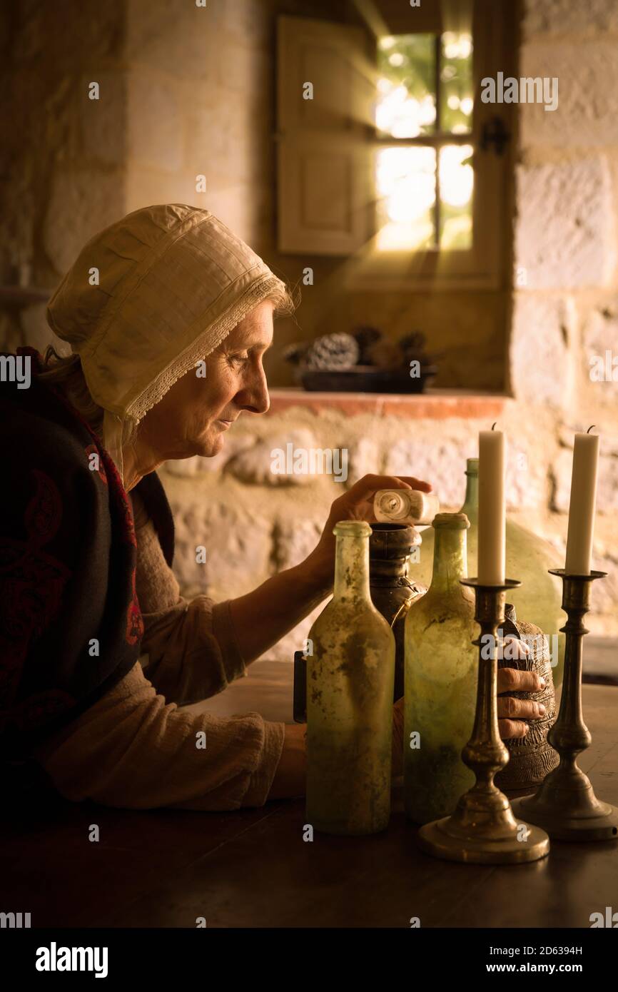 Femme en tenue médiévale travaillant comme un alchimiste ou une sorcière dans la cuisine d'un château médiéval français - avec des biens Banque D'Images