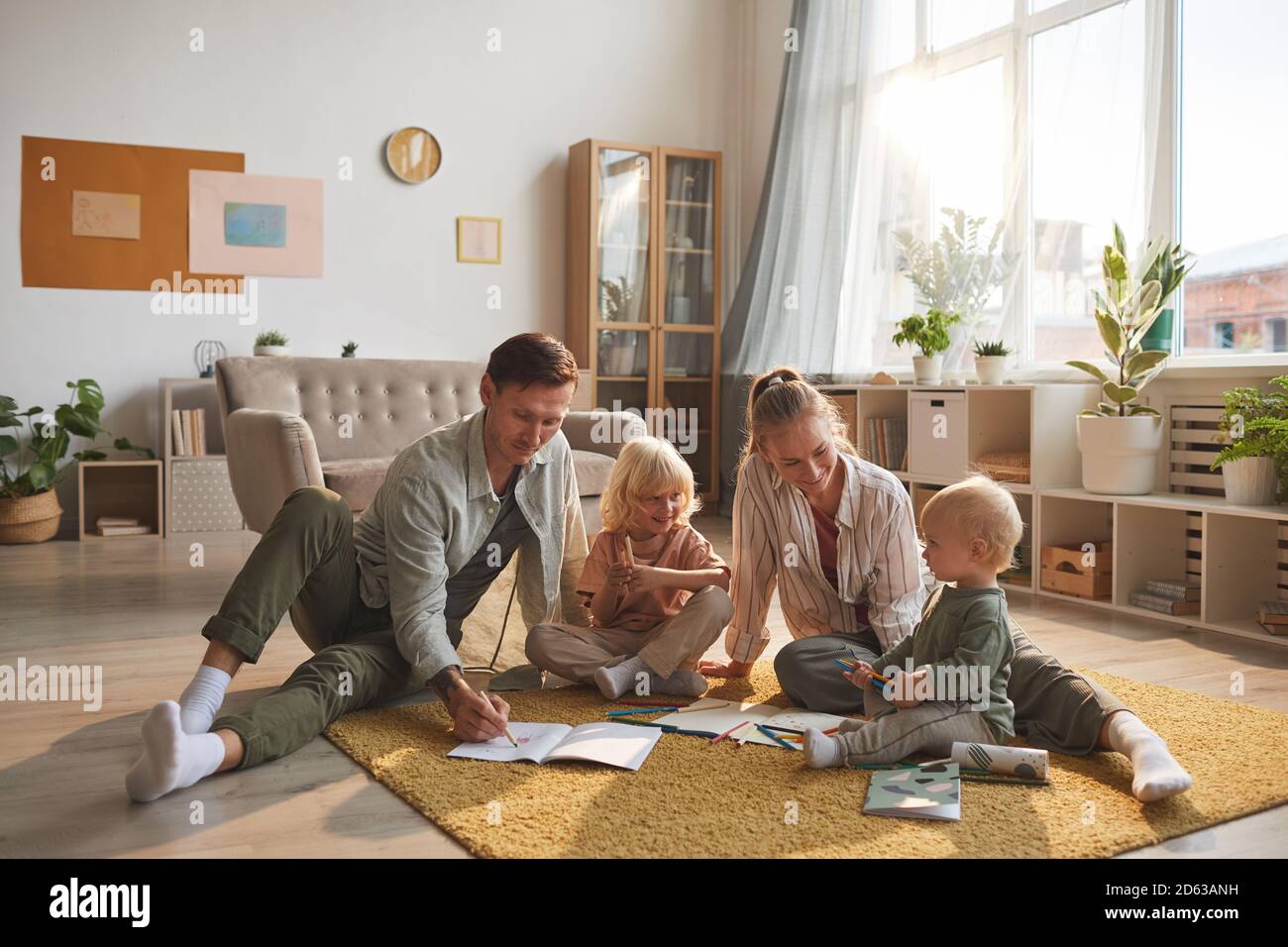 Deux parents dessinant sur le sol avec leurs deux enfants dans le salon Banque D'Images