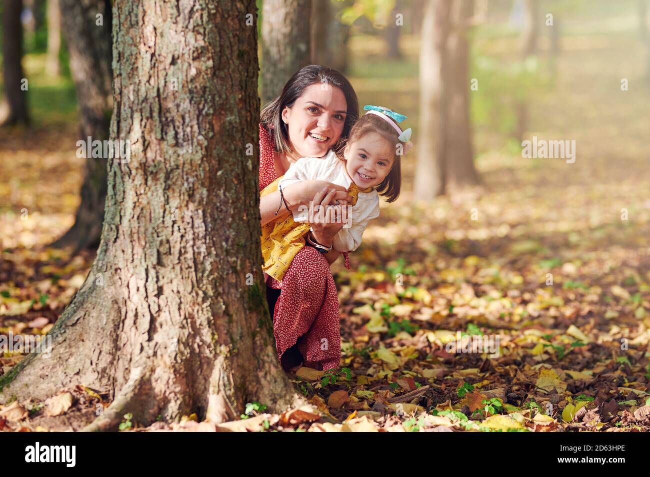 Maman avec sa fille jouer dans le parc d'automne se cacher derrière l'arbre Banque D'Images