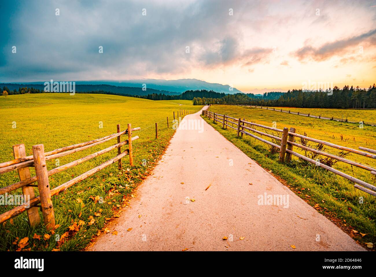 Route rurale dans le pays de la Bavière, Allemagne. Prairie verte et sentier en premier plan avec ciel spectaculaire au coucher du soleil et nuages en arrière-plan Banque D'Images