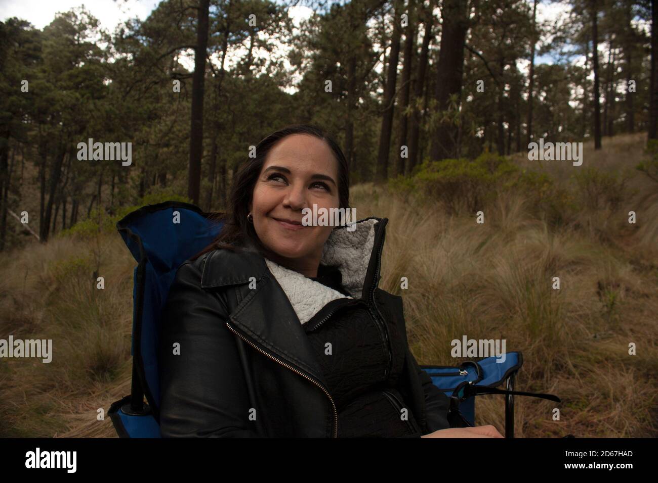 Femme souriante assise sur une chaise de camping au milieu de la forêt solitaire et heureux dans la nouvelle réalité Banque D'Images