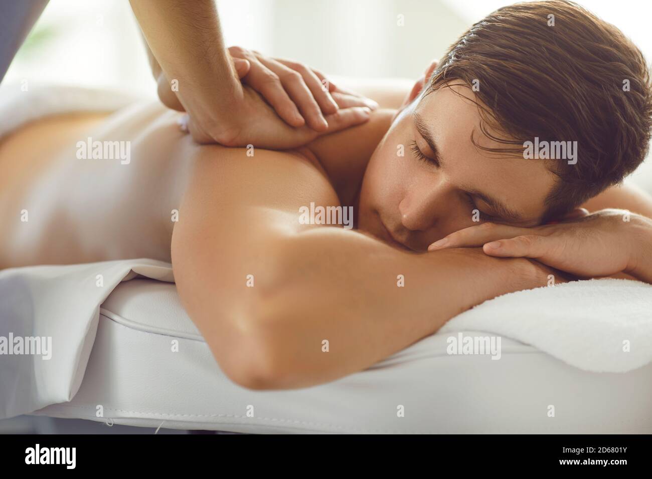 Jeune homme allongé sur une table de massage avec les yeux fermés appréciant massage relaxant professionnel du dos Banque D'Images