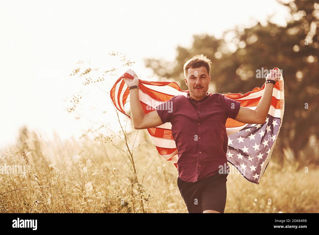 L'homme adulte court avec le drapeau américain dans les mains à l'extérieur dans le champ. Sensation de liberté sous un jour ensoleillé Banque D'Images