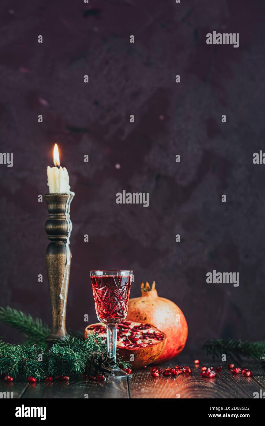 Accueil nourriture Noël et composition du nouvel an. Verre de grenade d'époque, boissons entourées de branches de pin et de bougies festives, fond sombre Banque D'Images