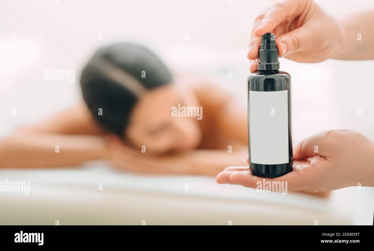Publicité pour un massage aromatique. Gros plan de l'huile de massage dans les mains d'un massothérapeute, en arrière-plan, une femme après le massage. Banque D'Images