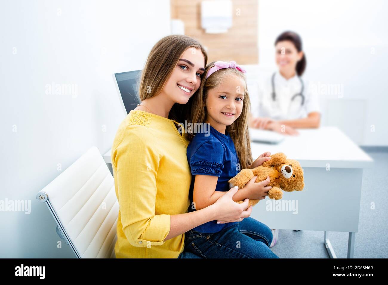 Portrait d'une petite fille heureuse assise dans les bras de sa mère à l'hôpital. Pédiatre en visite avec un parent, santé des enfants Banque D'Images