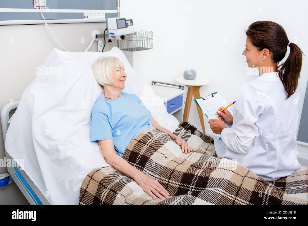 le médecin explique le rendez-vous de traitement en étant assis dans le lit d'hôpital d'un patient âgé. Réadaptation après une crise cardiaque, un accident vasculaire cérébral Banque D'Images