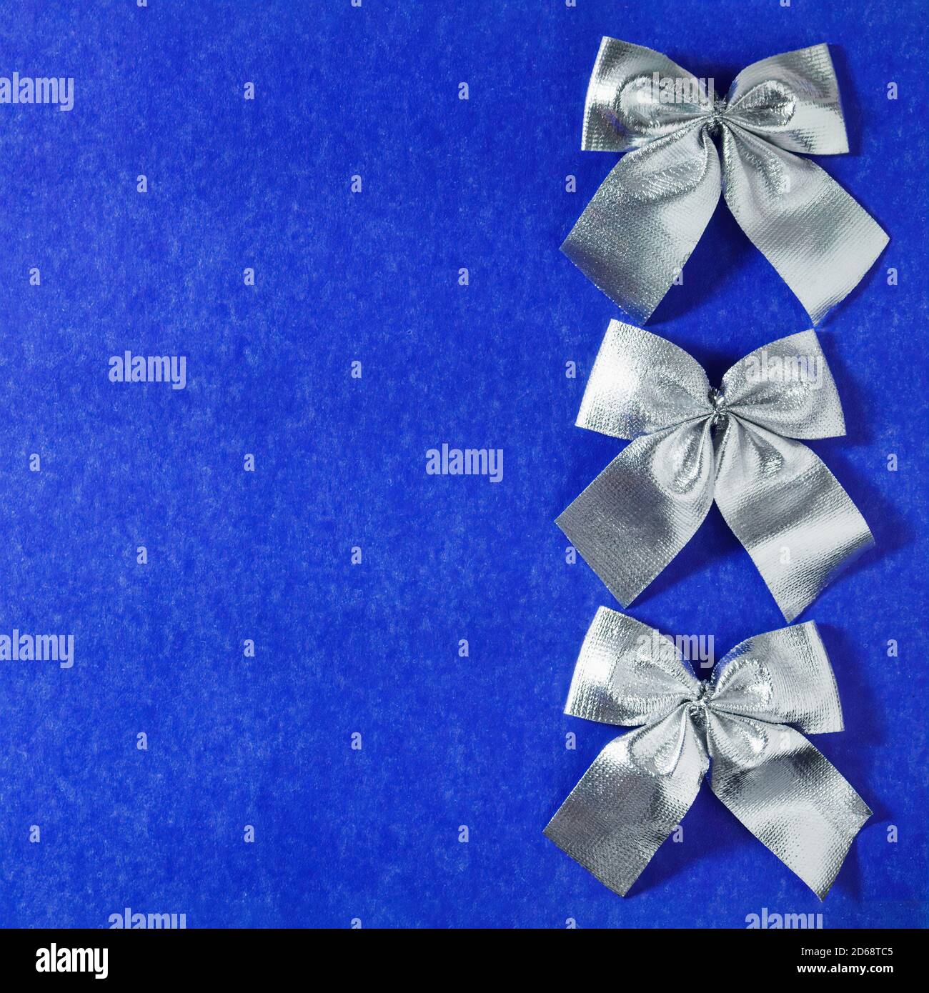 Trois noeuds décoratifs en argent en rangée sur fond de carton bleu. Vue de dessus, espace de copie pour le texte. Banque D'Images