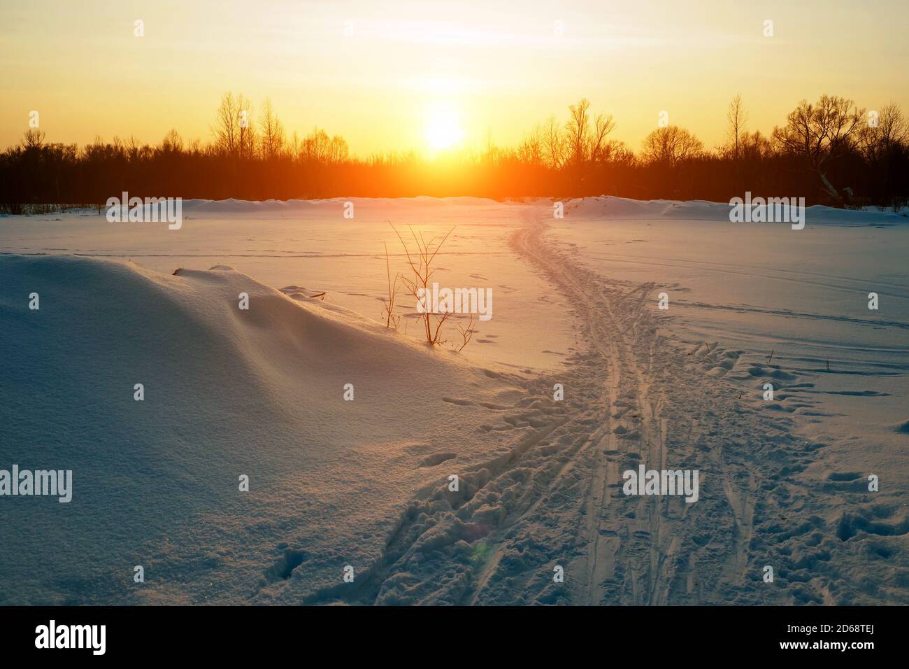 Piste de ski et sentier de randonnée dans un champ enneigé d'hiver, forêt et coucher de soleil sur le deuxième plan Banque D'Images