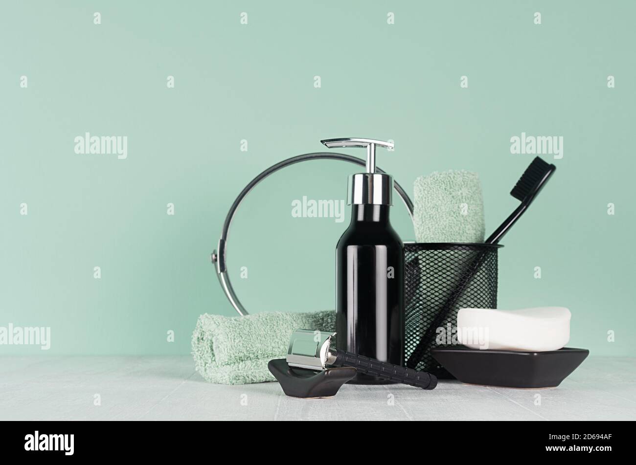 Intérieur de salle de bains élégant avec accessoires de rasage noirs sur mur vert, table blanche - rasoir, brosse à dents, miroir, serviette, savon, distributeur. Banque D'Images