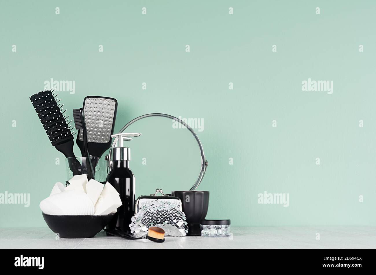 Articles de toilette noirs pour le nettoyage de la peau, soins de la peau - peigne noir, brosse, miroir rond, éponge, distributeur dans intérieur couleur menthe aqua, table en bois blanc. Banque D'Images