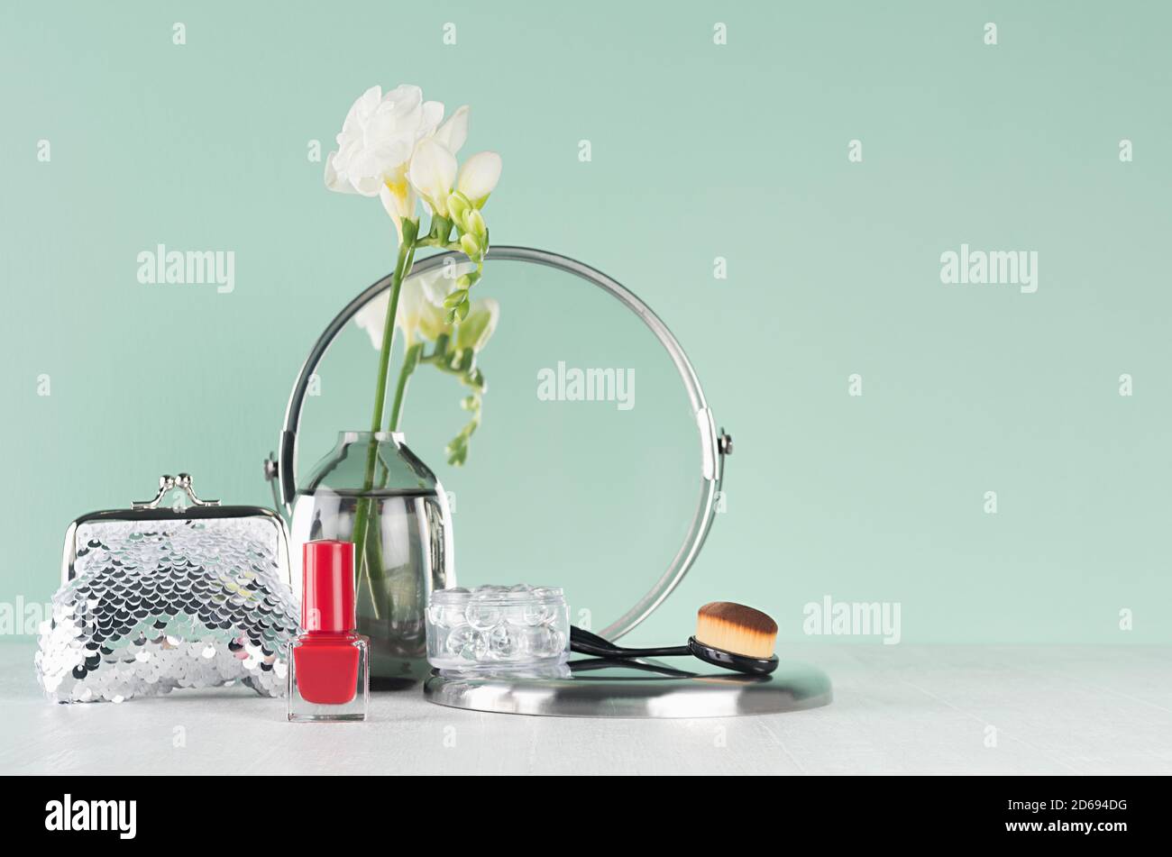 Cosmétiques et accessoires élégants en argent pour le maquillage - miroir rond, pinceau, fleurs blanches, vernis à ongles rouge, sac de cosmétiques à l'intérieur vert turquoise menthe Banque D'Images