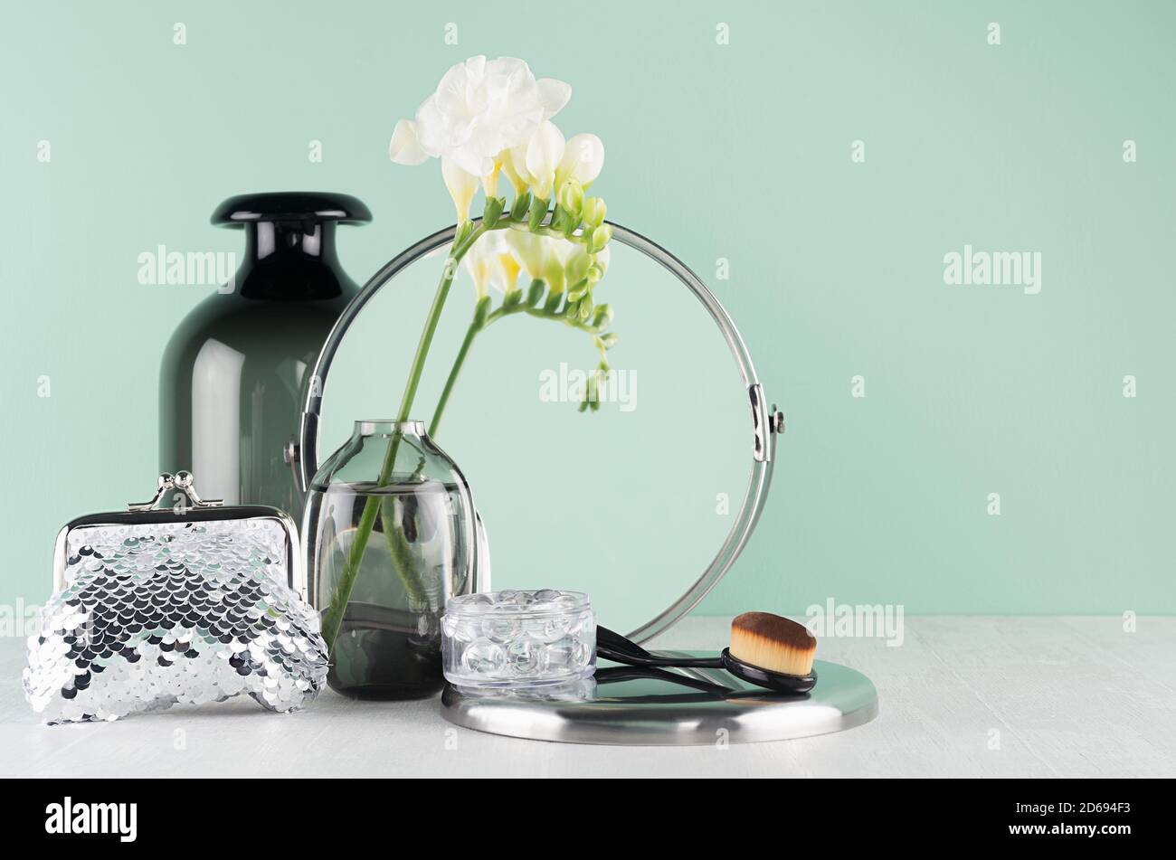 Table de maquillage de printemps avec accessoires cosmétiques pour le maquillage, nettoyage de la peau en argent, noir avec fleurs blanches, miroir rond sur bois blanc, hommes de menthe Banque D'Images
