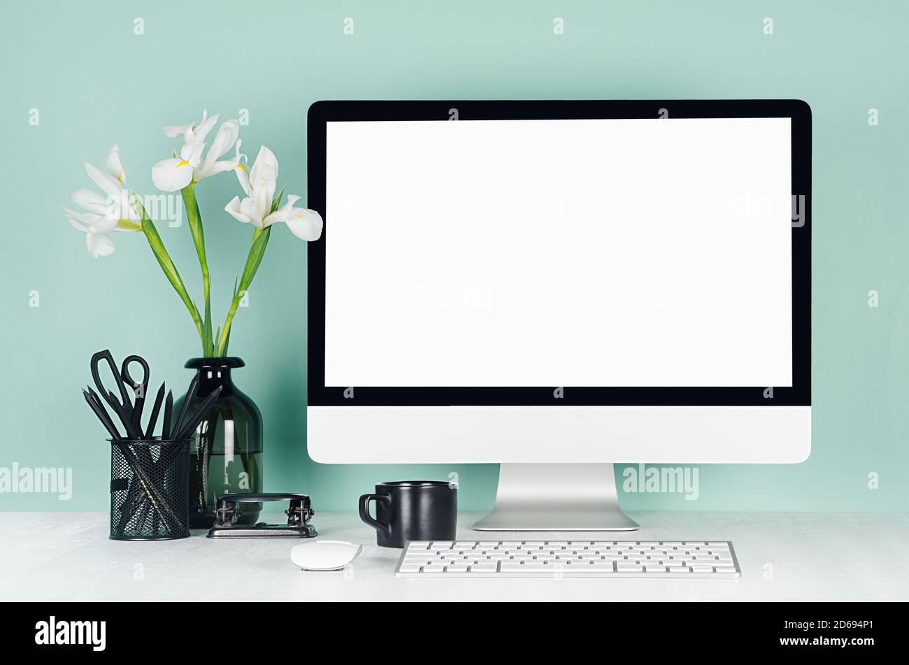 Intérieur de bureau minimaliste avec écran d'ordinateur vierge, papeterie noire, livres, fleurs blanches, clavier, tasse de café en menthe verte à l'intérieur o Banque D'Images