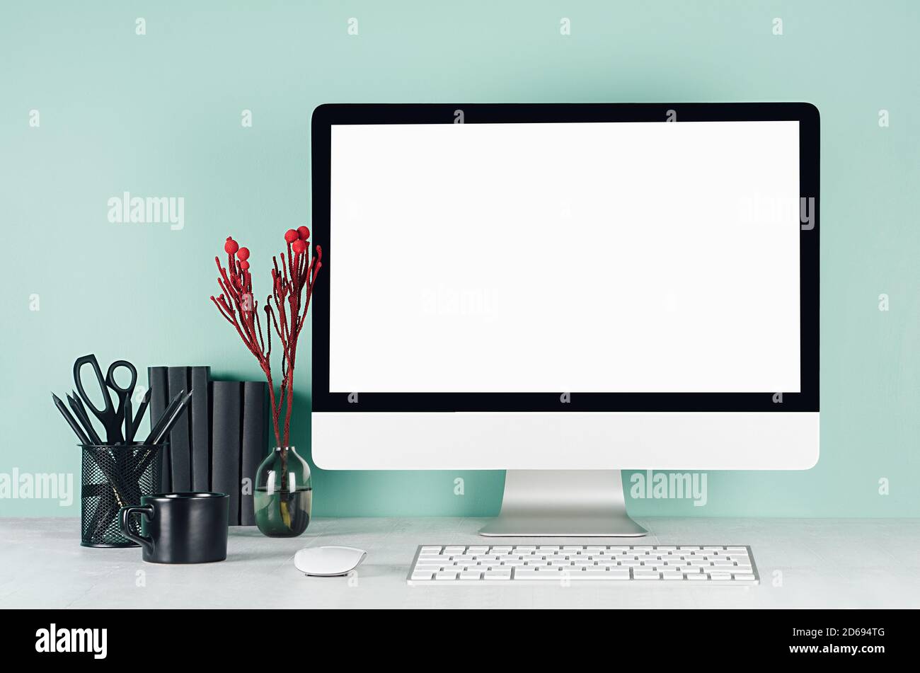 Intérieur de bureau simple avec moniteur d'ordinateur vierge, papeterie noire, livres, fleurs rouges, clavier, tasse de café en vert menthe menthe intérieur sur blanc Banque D'Images