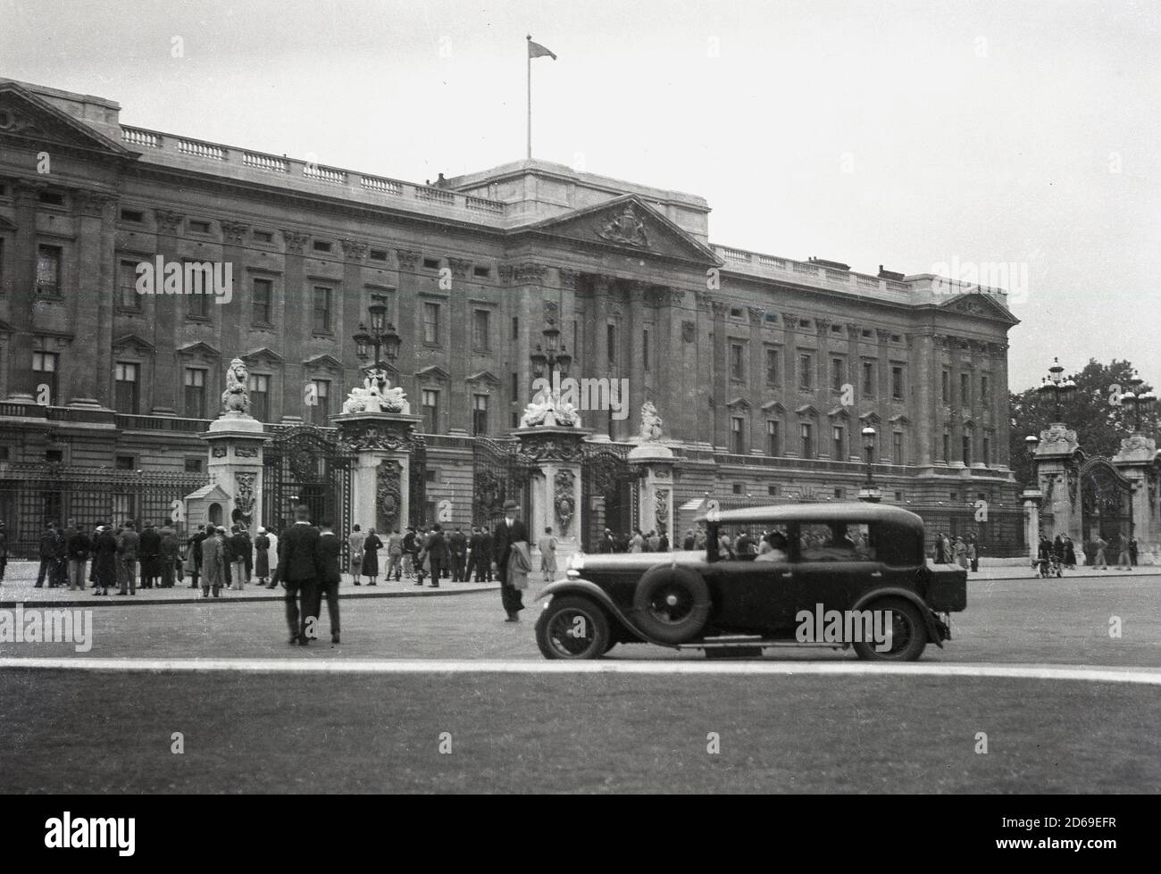 Années 1920, historique, une voiture à quatre portes de l'époque garée sur le Mall en face de Buckingham Palace, la résidence londonienne de la reine Elizabeth britannique. Les gens se tiennent à la clôture en fer forgé du palais, Londres, Angleterre, Royaume-Uni, dans l'ouverture d'un aperçu de la célèbre résidence royale. Banque D'Images
