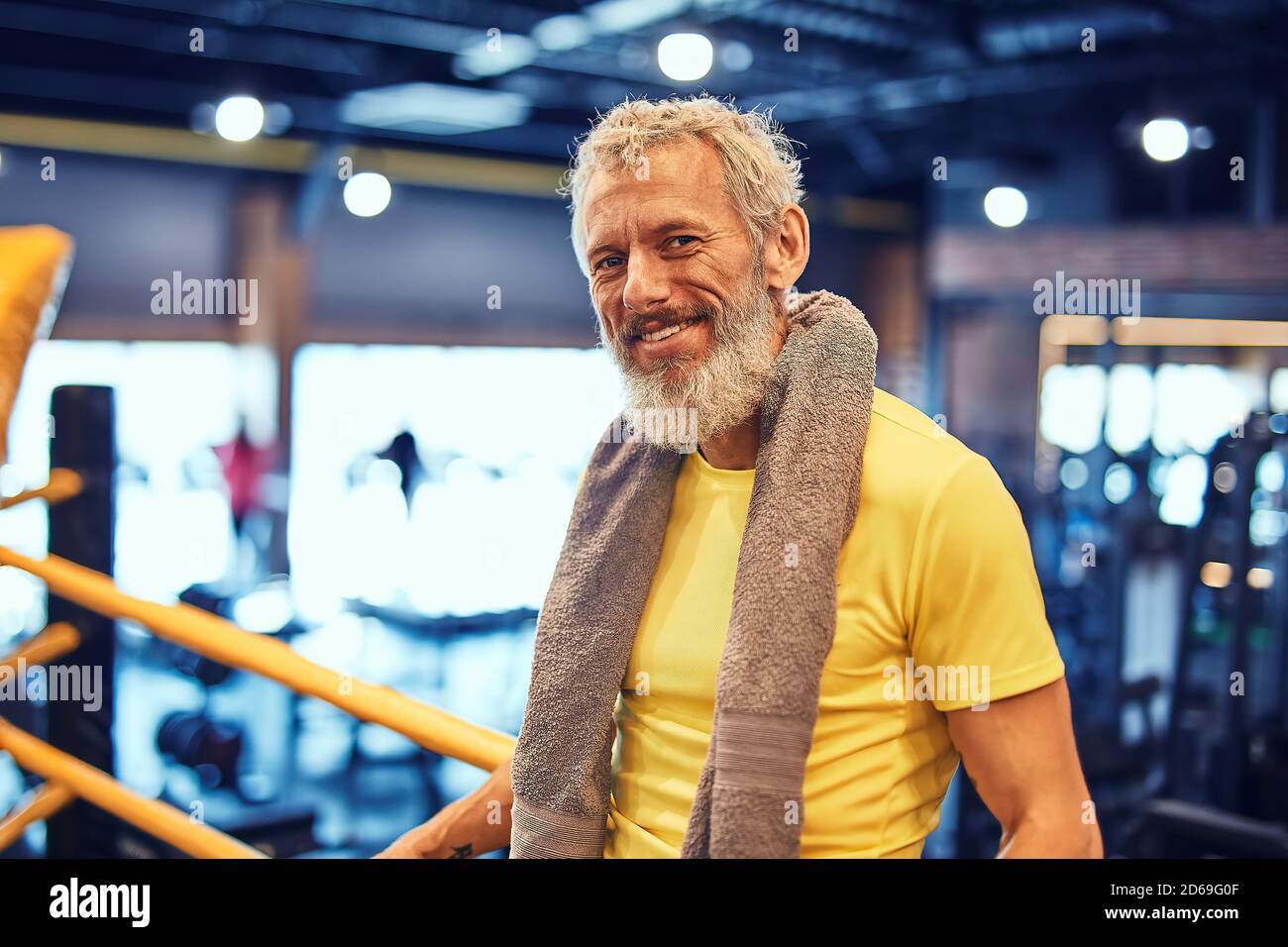 Repos après l'entraînement de boxe. Portrait d'un bel homme mûr positif en vêtements de sport regardant l'appareil photo et souriant en se tenant debout sur l'anneau à Banque D'Images