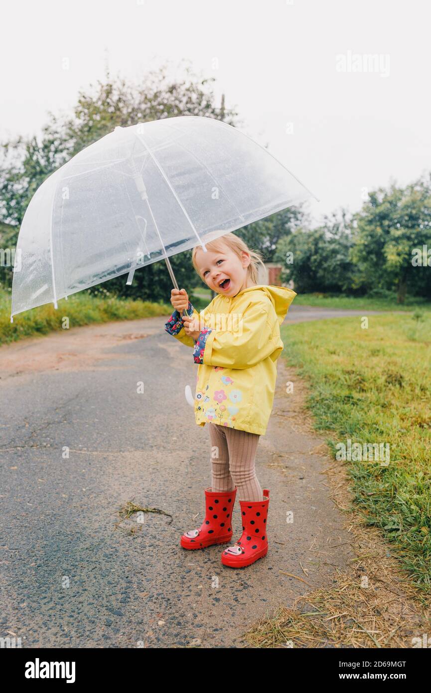 Petite fille drôle jouant dans le jardin sous la pluie d'automne. Enfant  portant un manteau imperméable jaune et des bottes tenant un parapluie  coloré. Temps pluvieux Photo Stock - Alamy